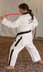 DSCF0021 2) Turn 90° to the left towards B, perform a middle section inner forearm block (middle block – knuckles down) with the left arm, hip-twisting into a left walking stance (bent front knee, straight back leg, heel on ground, weight 50/50, pivot on ball of left foot for hip twist )